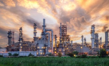 view of a large industrial complex with metal chimneys and scaffolding against a sunset sky